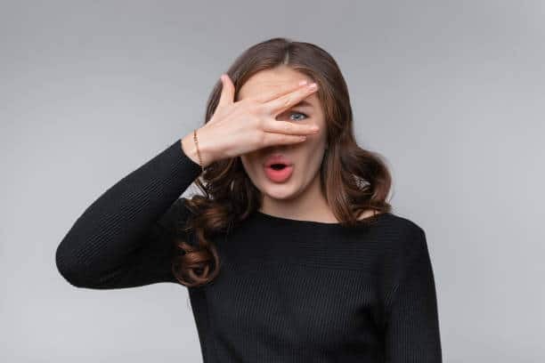 Woman covering her eye with hand, expressing surprise or shock, relevant to dental emergency situations.