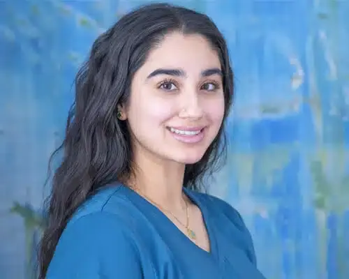 Smiling dental staff member in blue scrubs against blue background.