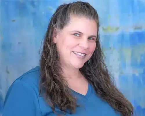 Smiling dental staff member in blue scrubs against blue background.