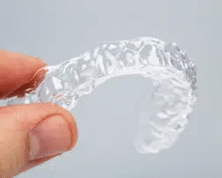 Clear dental retainer held in hand, showing transparent orthodontic device for teeth alignment.