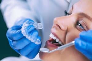 Dentist holding clear Invisalign aligner tray next to smiling patient's open mouth during consultation.