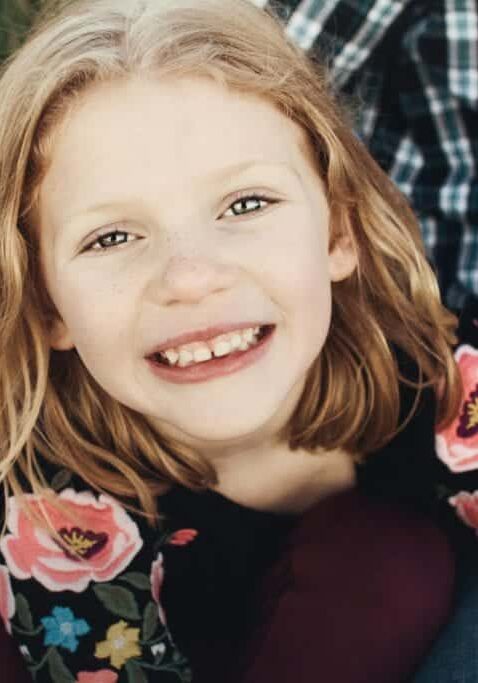 Smiling young girl with reddish-brown hair wearing a floral top during a family portrait session.